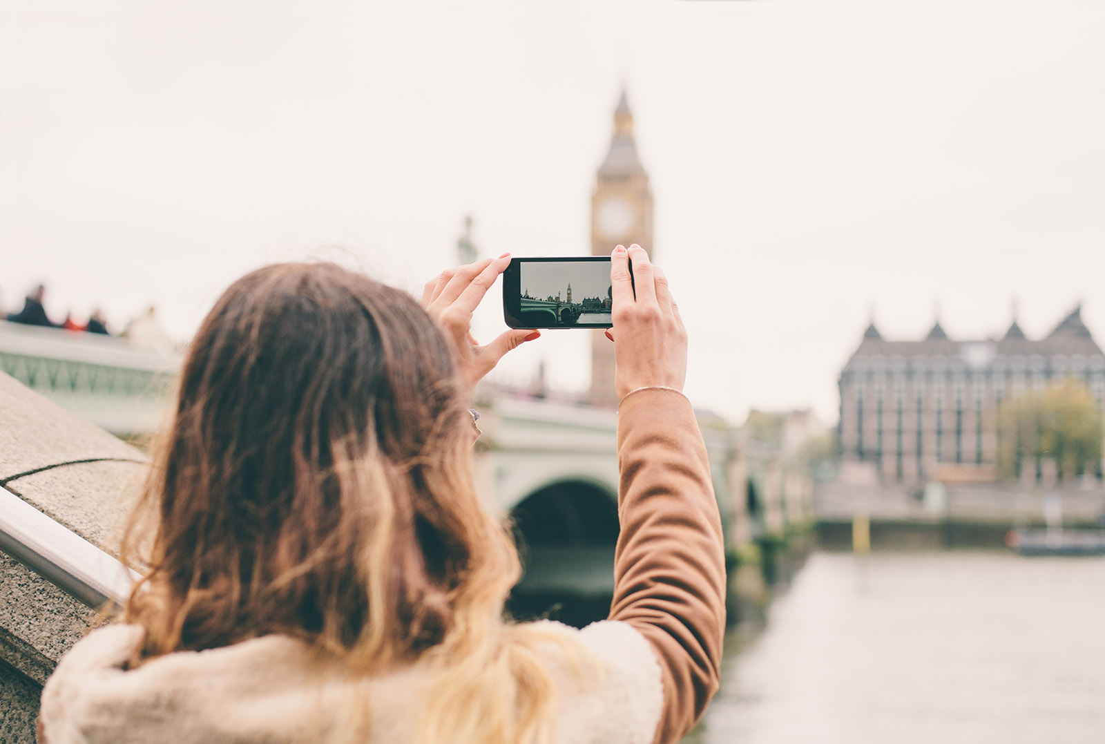 Create albums on your phone when travelling - Girl holding up mobile phone taking photograph of sites while travelling | BNE Traveller Tips: What to do with your holiday photographs