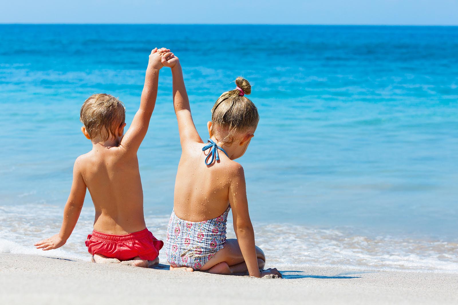 Gift your travel memories to a loved one - two young children holding hands up on the beach | BNE Traveller Tips: What to do with your holiday photographs