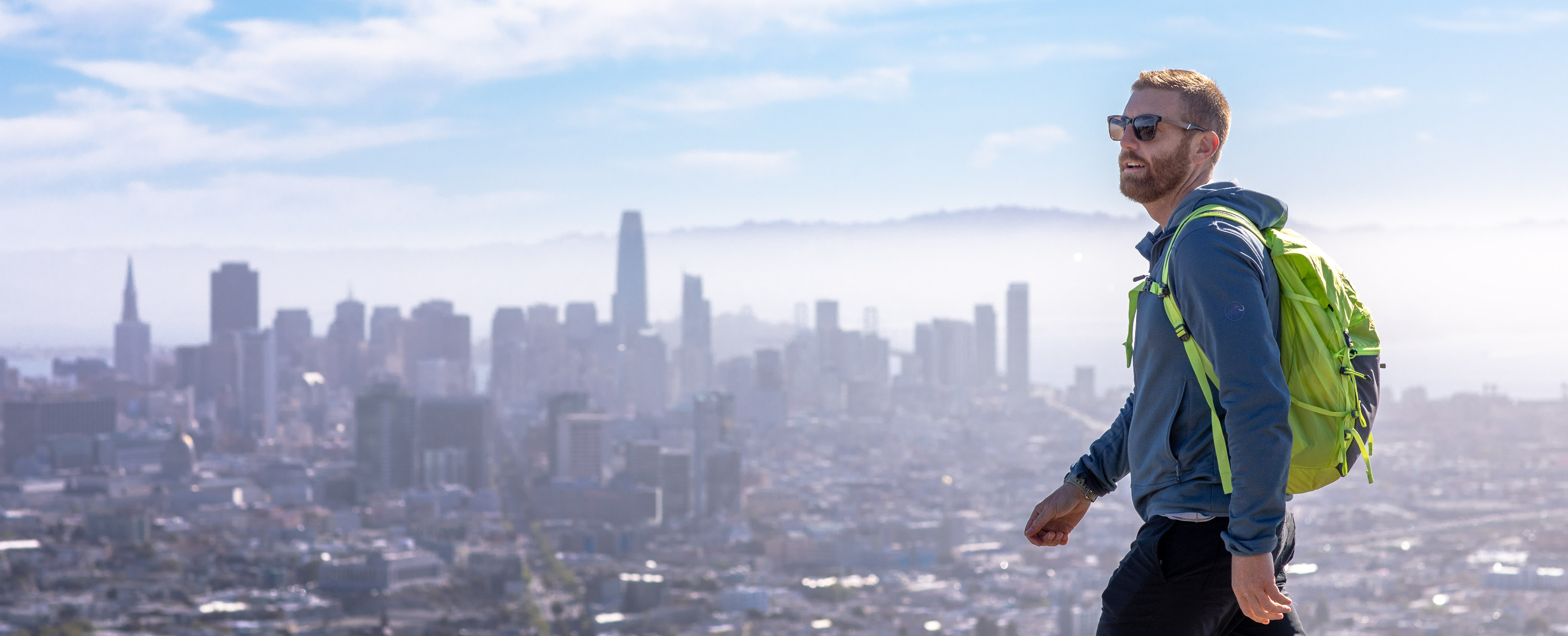 Man with backpack walking with San Francisco skyline in the background