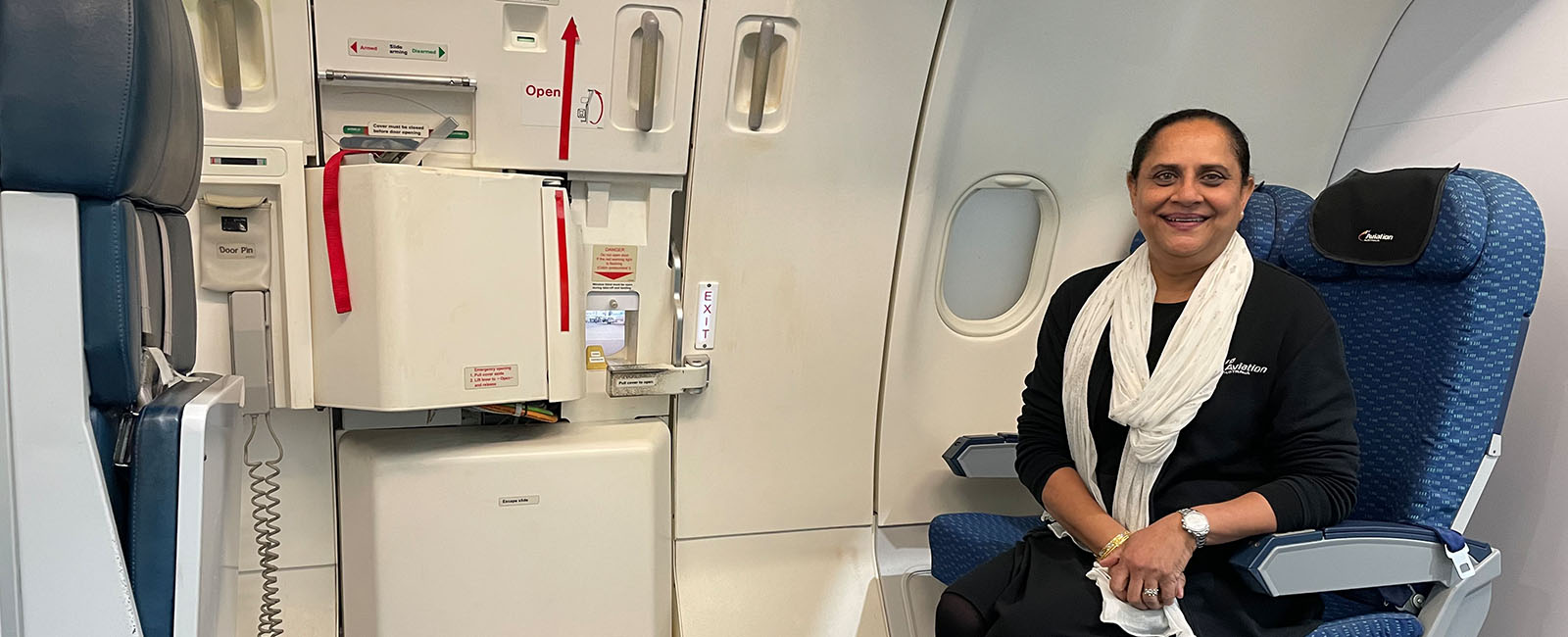 Harsha Patel sitting in an aircraft seat at an emergency exit. This is a training aid for cabin crew. 