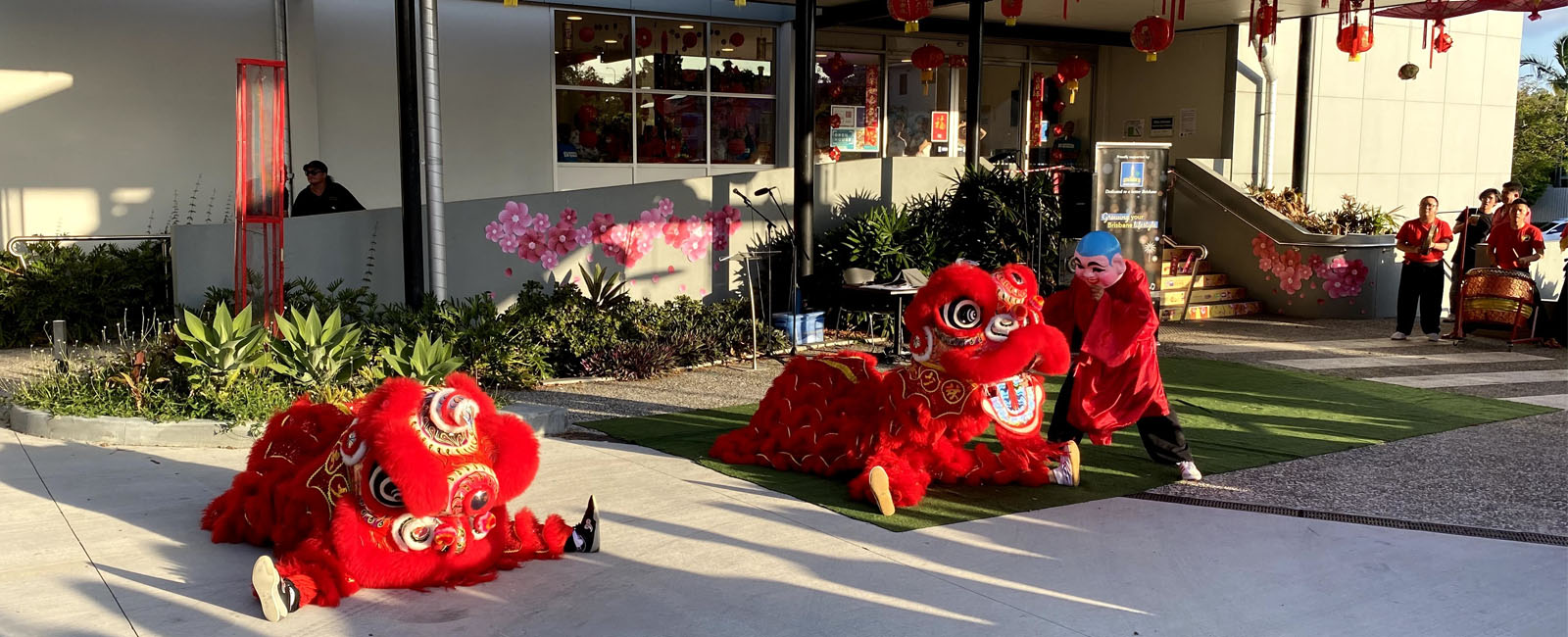 two chinese lion dancers crouch on the ground while a person dressed as buddha dances over them