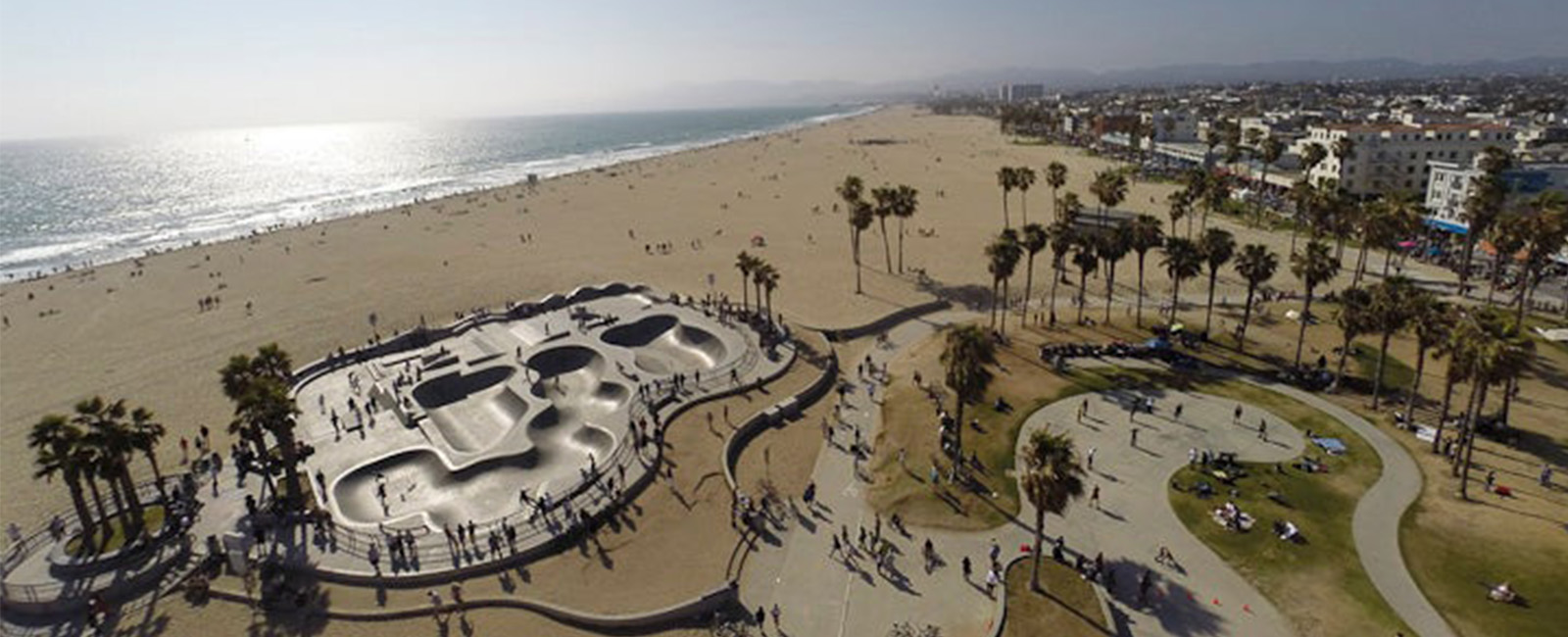 An aerial view of a skate park at a long flat sandy beach with the shimmering ocean in the background