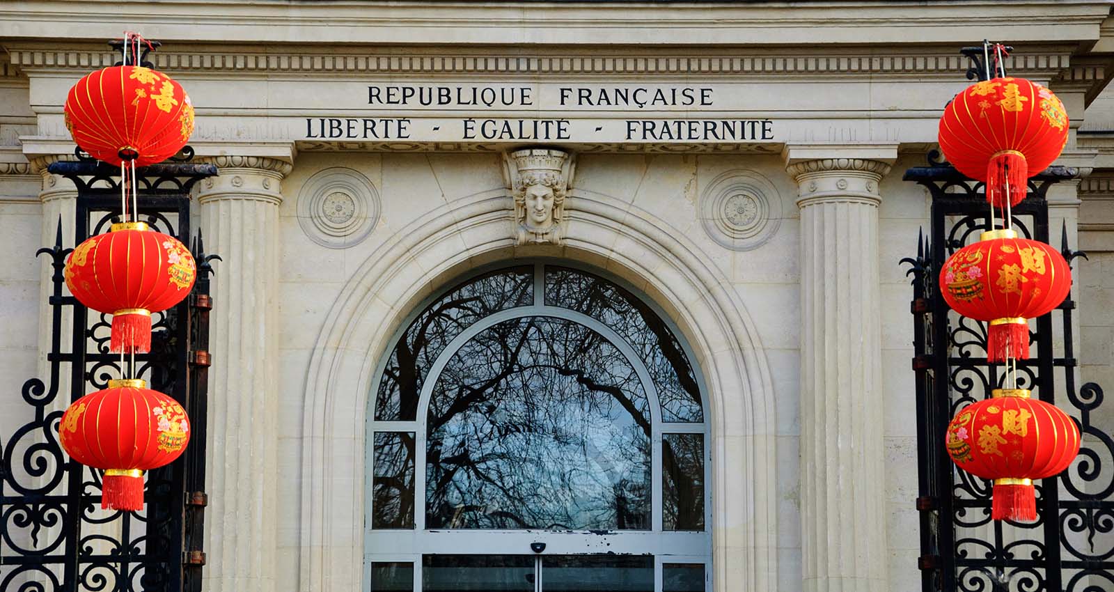 red lanterns hang infront of a french building with the words 'Liberte, egalite, fraternite' 