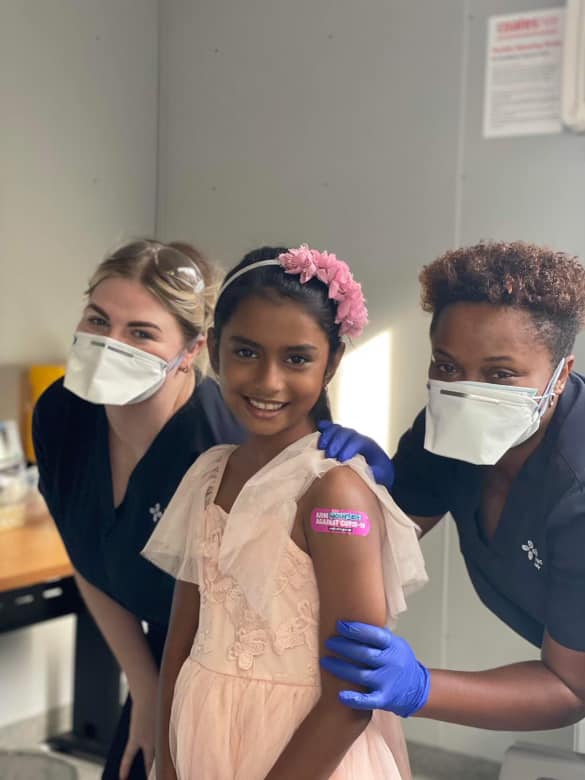 A child standing between two nurses who has just been vaccinated A child standing between two nurses who has just been vaccinated