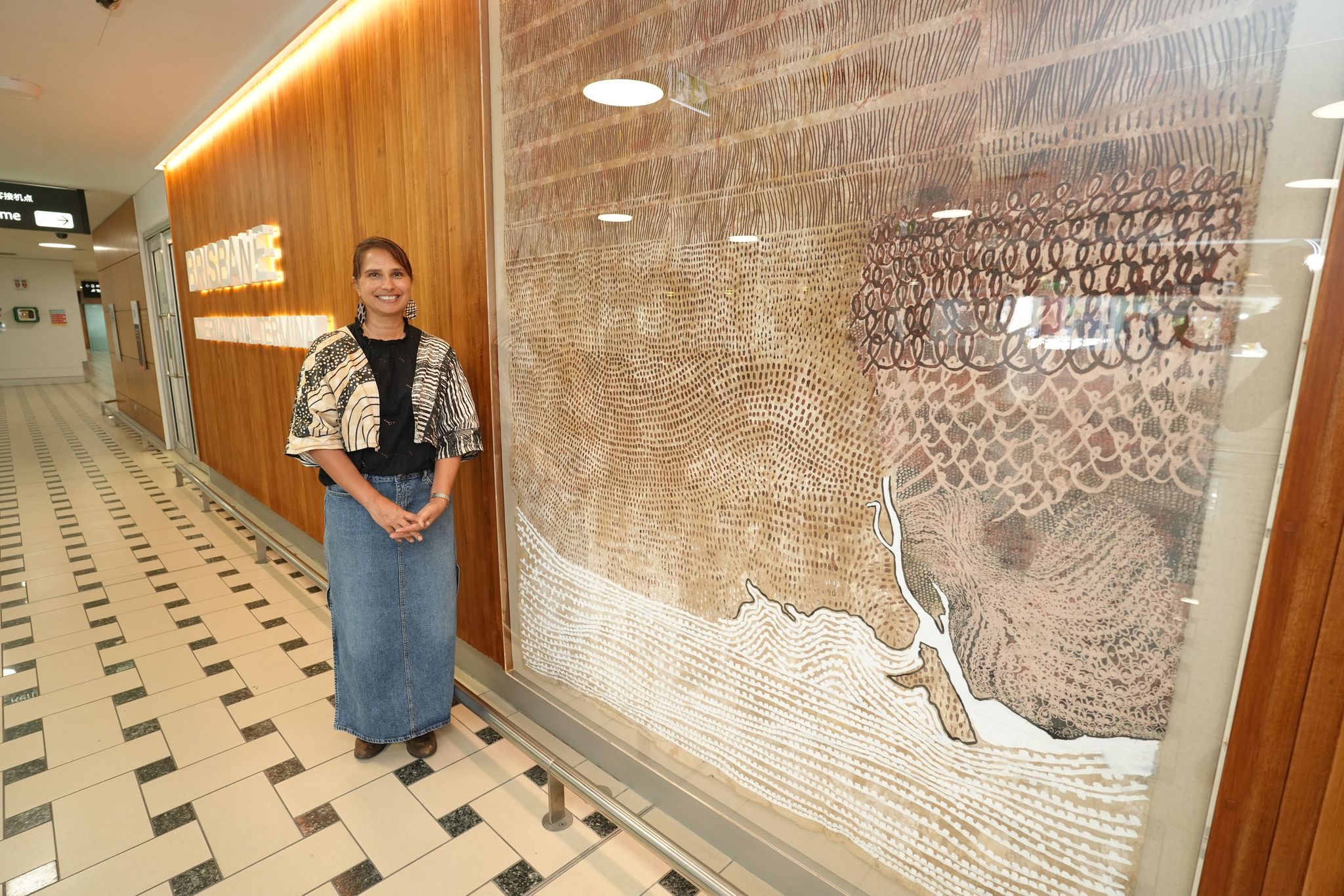 Delvene Cockatoo-Collins standing beside her artwork at Brisbane Airport