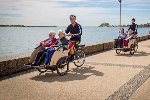two cyclists with elderly passengers cycling along a path near water