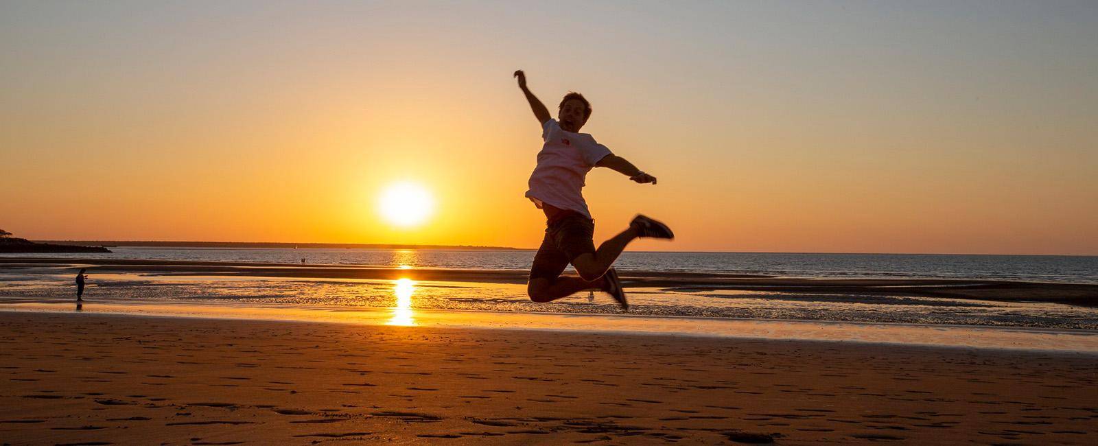 a person jumps for joy on a beach at sunset