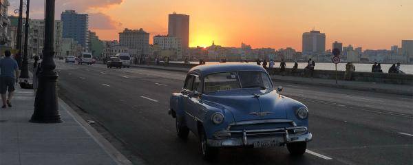 A vintage car on the road with the sun setting behind the city skyline