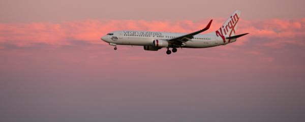 Virgin Australia aircraft arriving with pink skies behind it