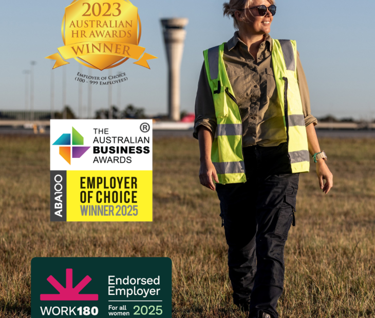 An airside operations officer walking with the air traffic control tower in the background.