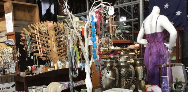 Photo from inside Op Shop with an assortment of second hand items - a purple dress on a mannequin, jewellery hanging on a stand and other bits and pieces. 