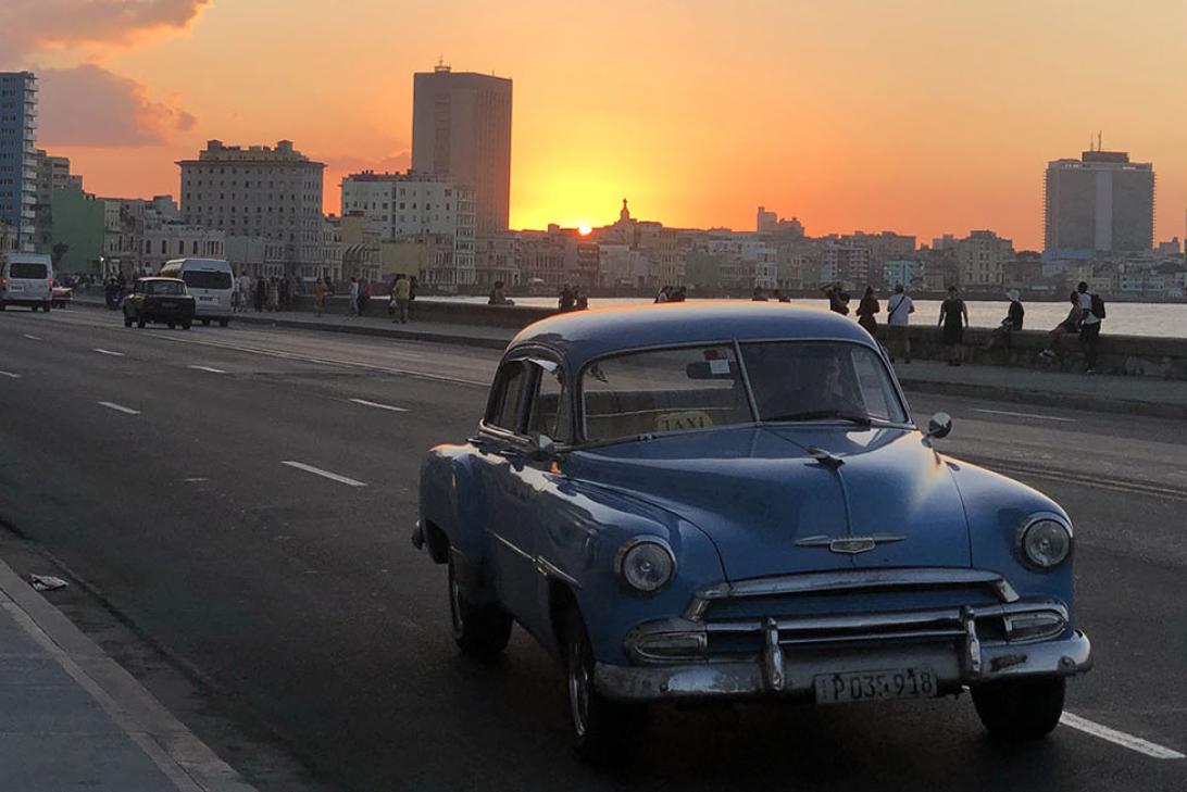 A vintage car on the road with the sun setting behind the city skyline