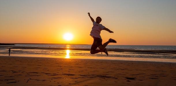 a person jumps for joy on a beach at sunset