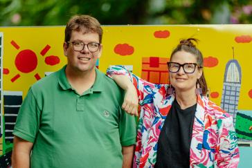 A man in a green shirt standing with a lady in a colourful jacket and black shirt