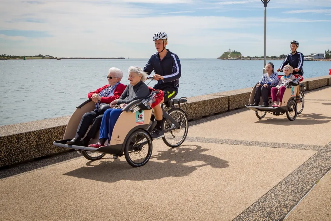 two cyclists with elderly passengers cycling along a path near water