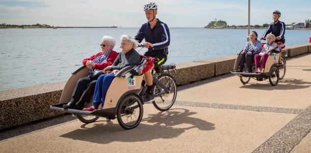 two cyclists with elderly passengers cycling along a path near water